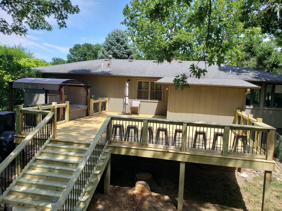 Large deck with wood handrails, black metal pickets, and wide custom stairs