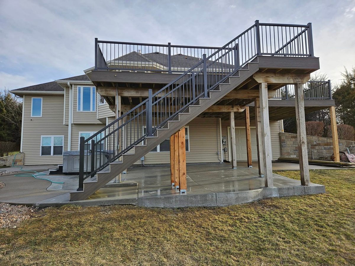 Large elevated deck with black metal railing above a concrete patio